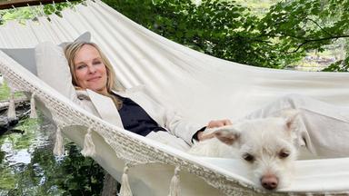 Bettina Rust, eine Frau mit langen blonden Haaren, liegt mit ihrem Hund in einer Hängematte.