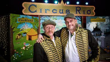 Zwei Männer Arm und Arm in einer Zirkusmanege.