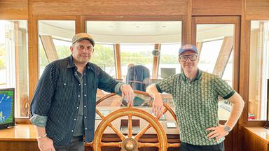 zwei Männer umrahmen einem Schiffsteuerrad