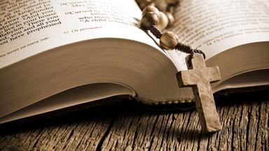 Auf einer aufgeschlagenen Bibel liegt ein Rosenkranz mit Kruzifix aus Holz.