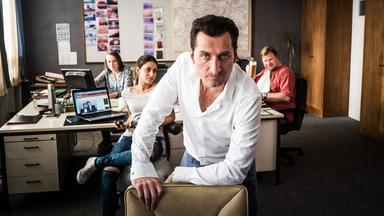 In einer Bürokulisse schaut ein Mann überlegen in die Kamera.