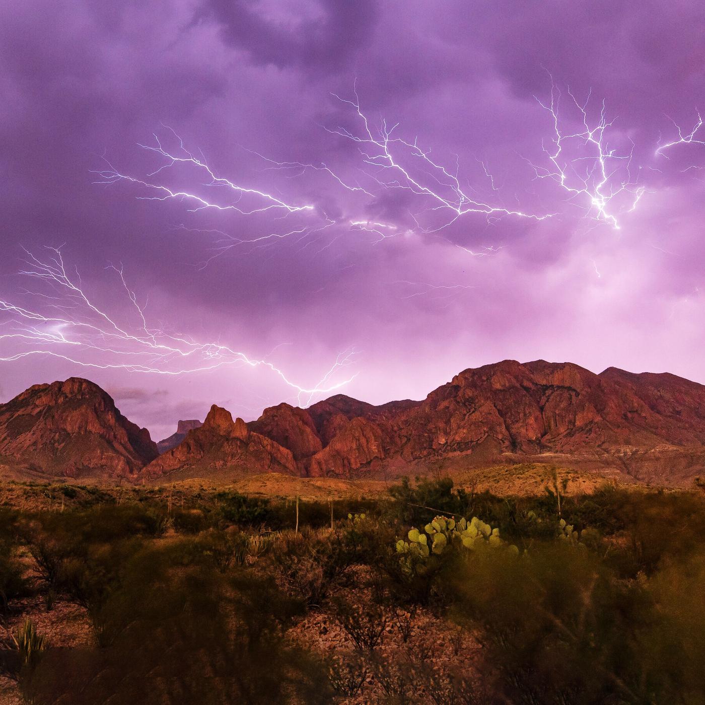 Ein lilafrabener Himmel mit weissem Blitzgewitter über einer Bergkette
