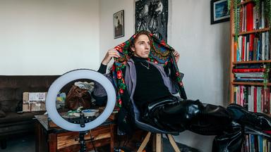 Daniel sitzt auf einem Stuhl und ist gerade dabei sich eine traditionell russische Kopfbedeckung zu binden.