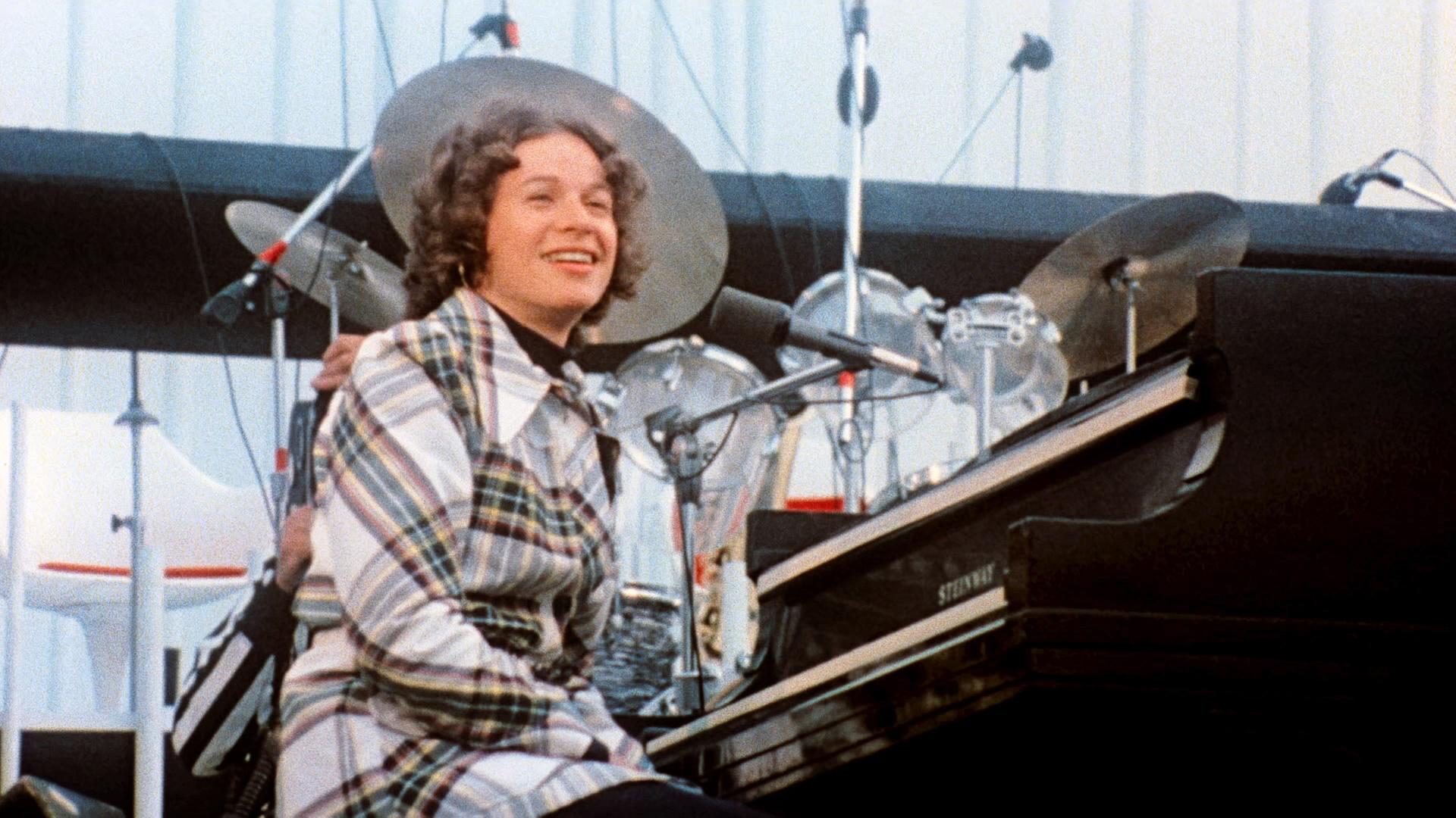 Carole King auf einer Bühne am Klavier.