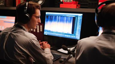 Mathieu (Pierre Niney) sitzt mit Kopfhörern und halb abgewandt von der Kamera vor einem Computerbildschirm, auf dem Grafiken einer Tonaufnahme zu sehen sind. Neben ihm sitzt, nicht vollständig sichtbar, ein männlicher Kollege, der ebenfalls Kopfhörer trägt.