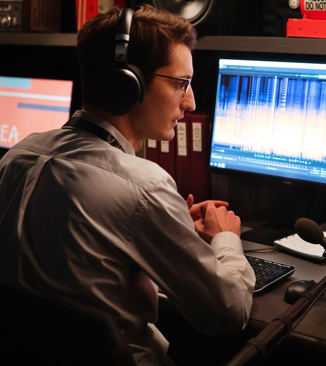Mathieu (Pierre Niney) sitzt mit Kopfhörern und halb abgewandt von der Kamera vor einem Computerbildschirm, auf dem Grafiken einer Tonaufnahme zu sehen sind. Neben ihm sitzt, nicht vollständig sichtbar, ein männlicher Kollege, der ebenfalls Kopfhörer trägt.