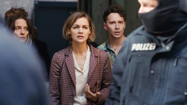 Die Nachbarn Henrike Koch, Caroline Hahn und Elias Levy schauen besorgt auf einen maskierten Polizisten, der in ihrem Hinterhof im Einsatz ist.