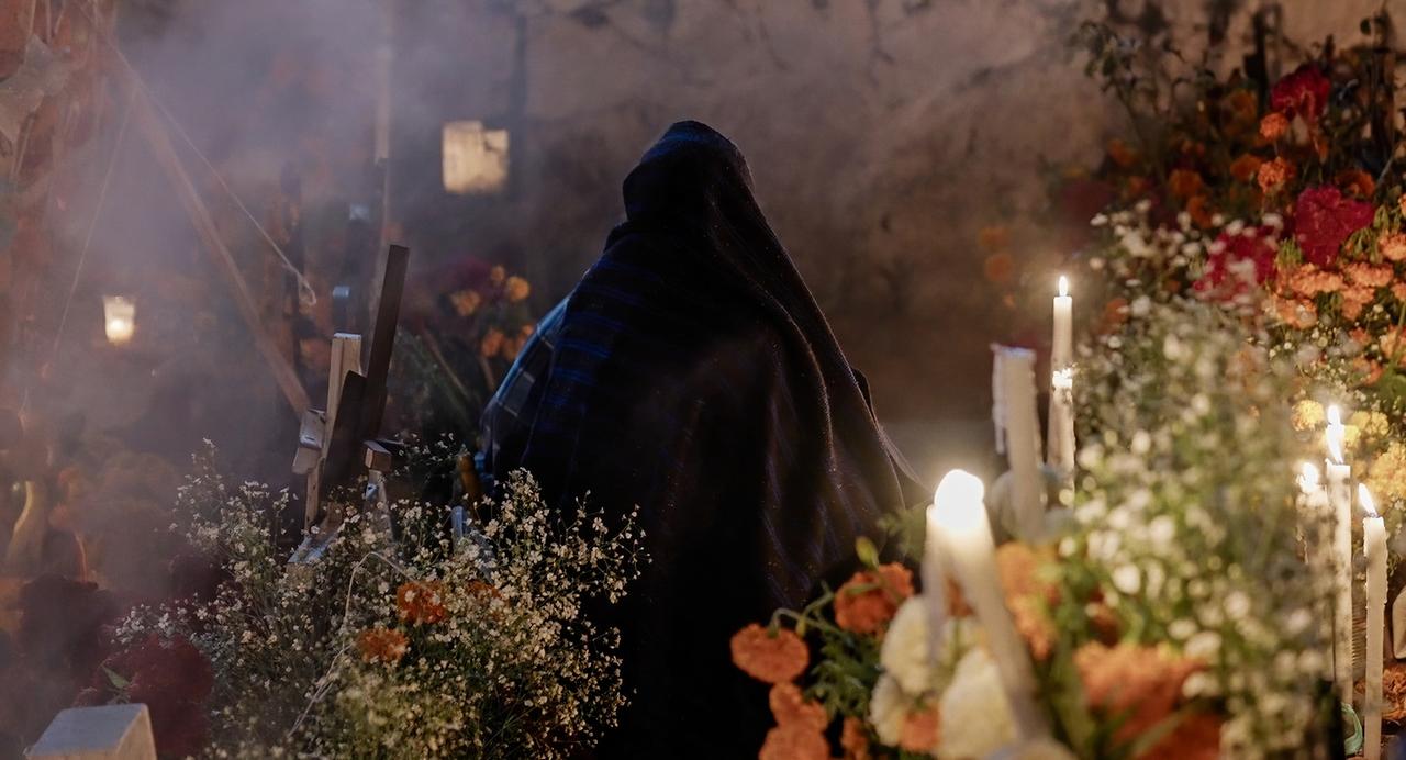 Eine verhangene Frau an einem Grab mit vielen Blumen.