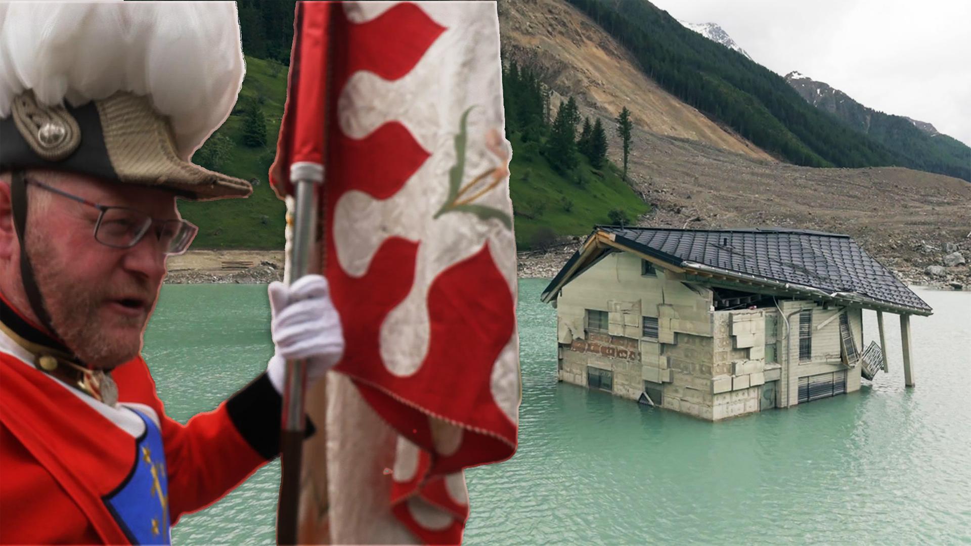 Das Bild zeigt mehrere Häuser, die teilweise im Wasser stehen. Es gibt zwei Häuser, von denen eines deutlich ausgeprägte Wände hat, die aus Beton oder ähnlichen Materialien bestehen. Das andere Haus sieht etwas moderner aus, mit einem Satteldach und großen Fenstern.   Das Wasser ist klar und hat eine grüne Färbung. Im Hintergrund sind sanfte Hügel und Berge zu sehen, die teilweise bewaldet sind. Der Himmel ist bewölkt, was eine trübe Stimmung vermittelt. Am Ufer sind geröllige Flächen zu erkennen, die auf Erdrutsch oder Bergbau hindeuten. Es gibt keine Personen oder Tiere im Bild, außer einen Mann der im Vordergrund zu sehen ist.