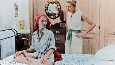 Cécile (Jean Seberg) sitzt mit einem Handtuch um den Kopf auf einem Bett, während Anne (Deborah Kerr) hinter ihr steht und sie mahnend anspricht.