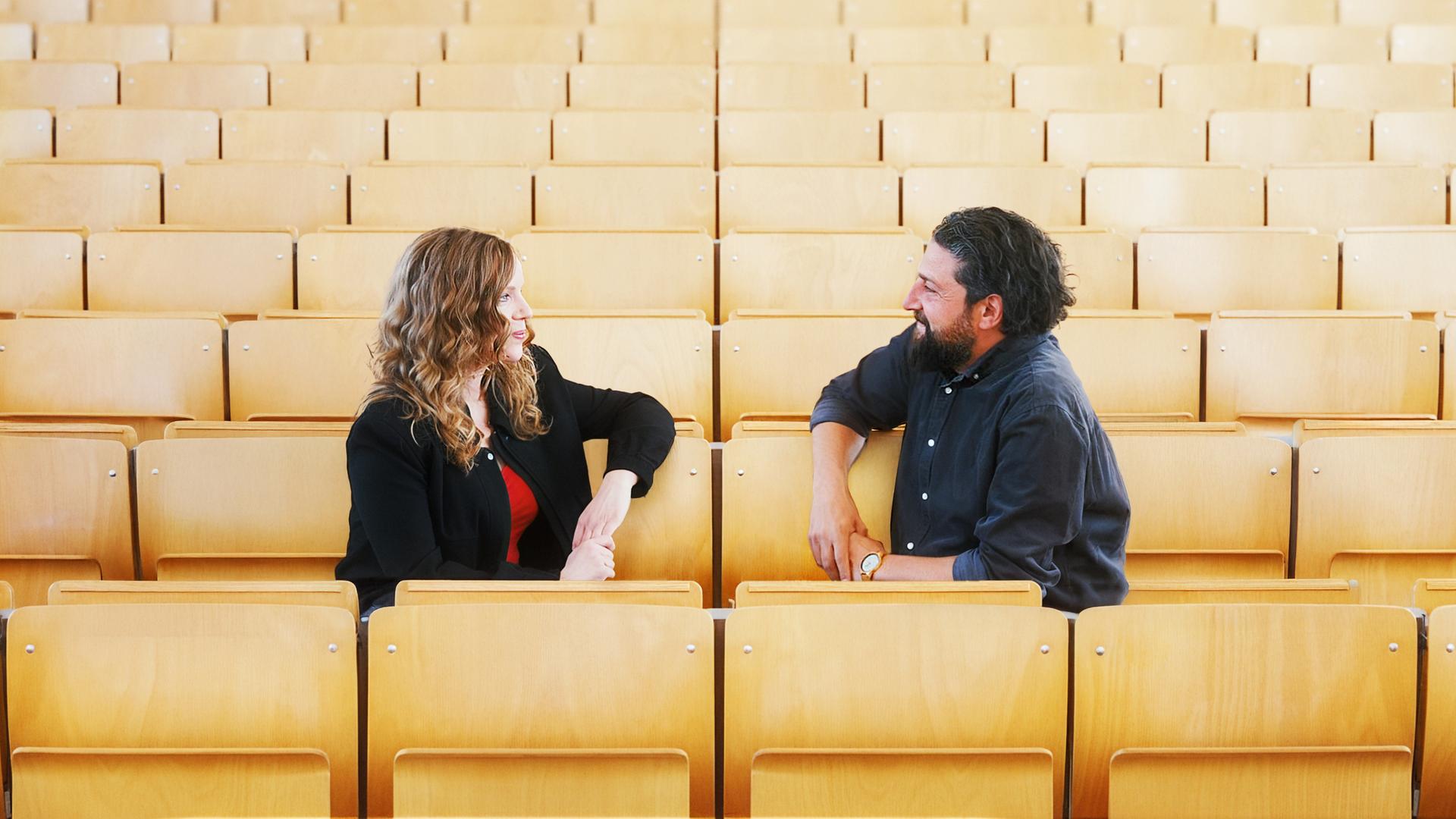 Sarah Bosetti sitzt auf der linken Bildseite. Auf der rechten Seite sitzt Aladin El-Mafaalani. Es sind Stuhlreihen abgebildet. 