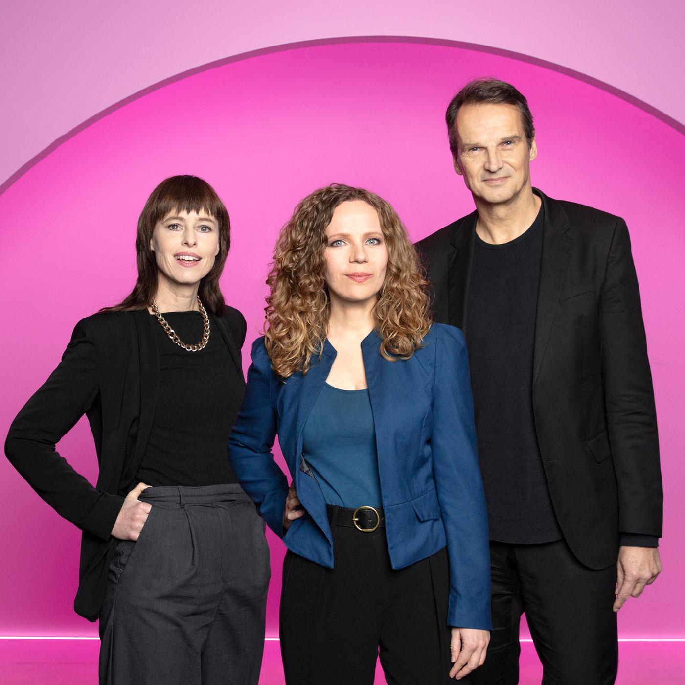 Auf dem Bild ist Sarah Bosetti mittig zu sehen. Links neben ihr steht die Historikerin Hedwig Richter, rechts neben ihr der Journalist und Autor Klaus Brinkbäumer. Der Hintergrund ist pink.