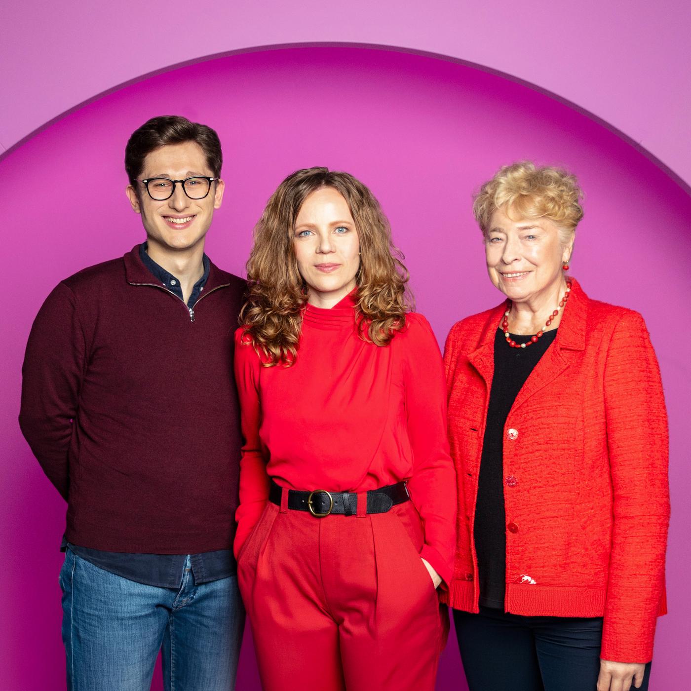 Sarah Bosetti steht in der Mitte des Bildes. Der Hintergrund ist rosa. Es sind drei Personen abgebildet. Links steht Philipp Türmer und rechts Gesine Schwan.