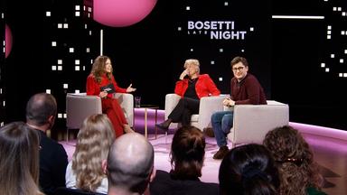 Sarah Bosetti sitzt auf einem Sessel im Studio. Es sind Köpfe am unteren Bildrand zu sehen. Der Hintergrund ist dunkel.