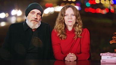 Auf dem Bild ist Sarah Bosetti auf der rechten Seite zu sehen. Links neben ihr sitzt Torsten Sträter. Beide sitzen hinter einen Schreibtisch.