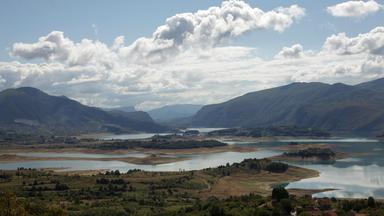 Blick auf den Ramsko jezero mit kleinen Inseln, umliegenden Bergen und bewölktem Himmel.