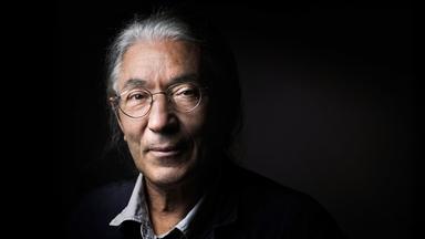 Porträtfoto eines Mannes mit grauen Haaren vor schwarzem Hintegrund.