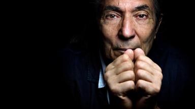 Nahaufnahme des Gesichts eines älteren Mannes der sich die Fäuste vor den Mund hält.