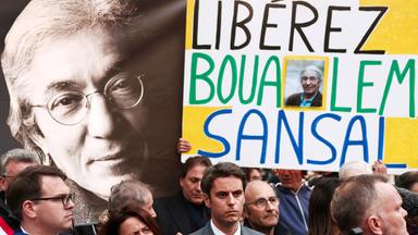 Menschen mit Plakaten stehen vor einem großen Bild des Schriftstellers.