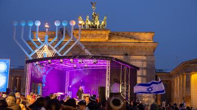 Vor dem Brandenburger Tor ist ein riesiger achtarmier Leuchter mit Davidstern aufgestellt. Eine Menschenmenge mit Israel-Flaggen hat sich vor einer Bühne vor dem Tor versammelt.