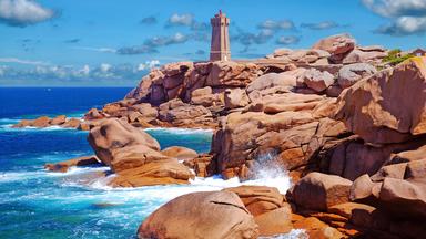 Ein Leuchtturm an einer Küste mit rosa Granitfelsen.