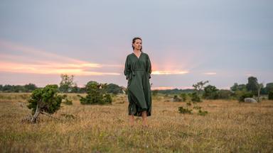 Eine Person steht in offener Landschaft mit weitem Himmel und natürlicher Umgebung; ruhige, weiträumige Szene.