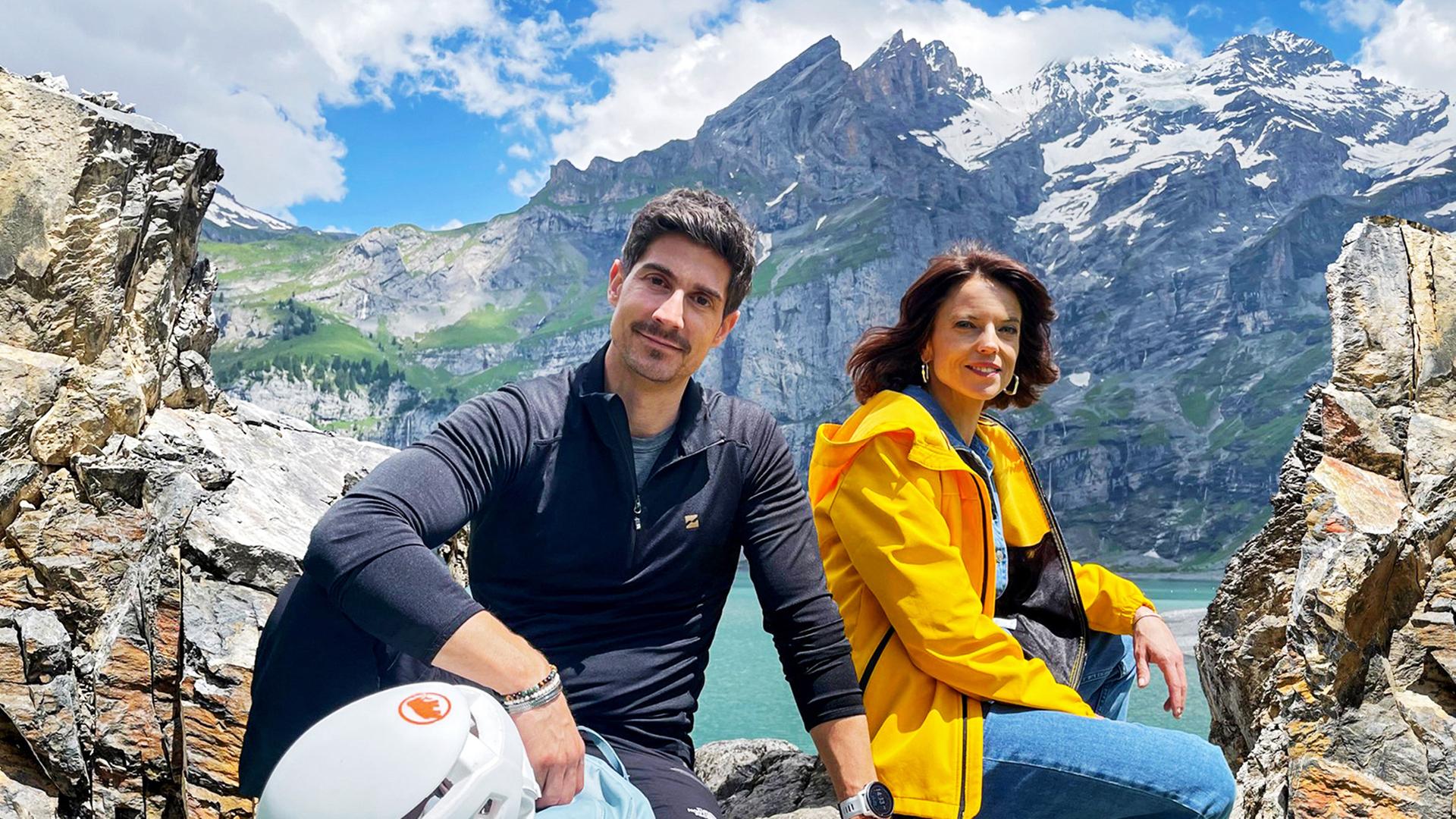 Mona Vetsch und Tobias Müller stehen am Oeschinensee oberhalb von Kandersteg, umgeben von einer beeindruckenden Berglandschaft. 