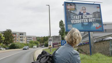 Rückansicht einer Frau vor einem großen Wahlplakat.