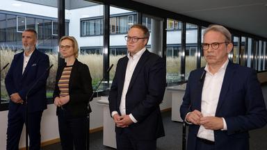Vier Personen stehen vor einer Glasfront.