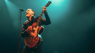 Bryan Adams singt mit einer Gitarre auf der Bühne.