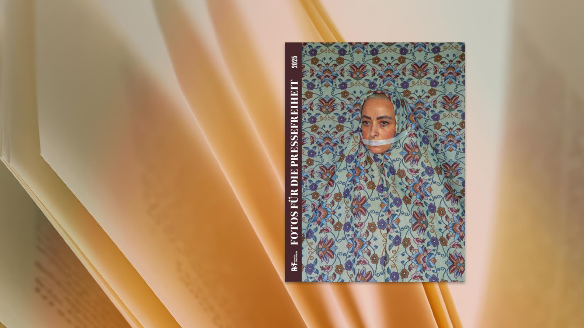 Eine Frau, die einen Klebestreifen über dem Mund trägt, sitzt vor einer gemusterten Tapete. Ihr Gewand hat das gleiche Muster wie die Tapete.