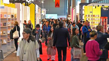 Auf der Buchmesse bewegen sich viele Menschen in den Gängen zwischen den Ständen.