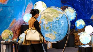 Frau betrachtet Globen an einem Stand auf der Frankfurter Buchmesse