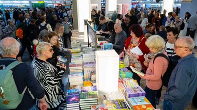 Auf der Buchmesse Leipzig stehen viele Menschen um lange Büchertische und blättern in Büchern.
