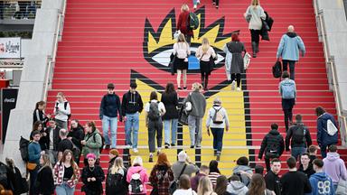 Menschen laufen eine rote Treppe mit dem gelben Logo der Buchmesse Leipzig hoch.