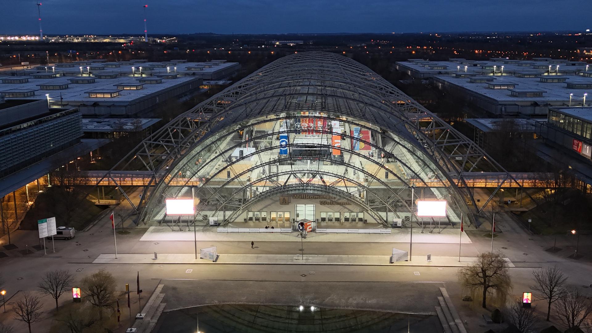 Blick auf die beleuchtete Kopfseite einer langen gewölbten Glashalle bei Nacht.