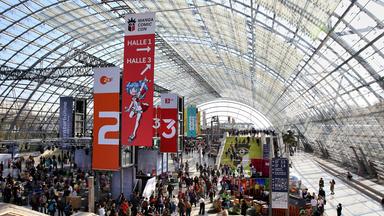 Eine große Menschenmenge wuselt in einer Glashalle über zwei Stockwerke. Im Hintergrund hängen Banner von ARD, ZDF, 3sat und arte.