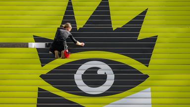Eine Frau klebt den letzten Streifen des Logos der Leipziger Buchmesse auf eine große Treppe.