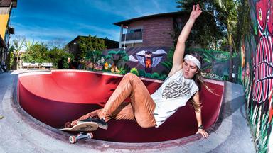 Eine Frau skatet in einer Bowl. Im Hintergrund sind Häuser zu sehen.