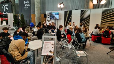 Junge Menschen warten sitzend am Messestand