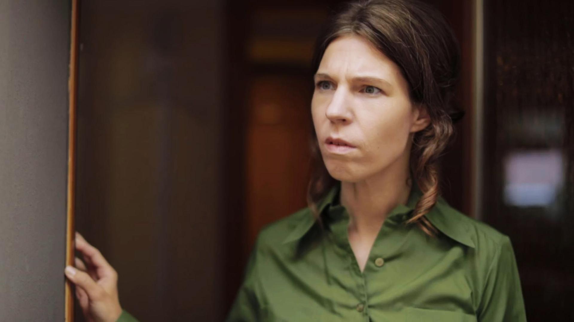 Szene aus "Long Island" von Colm Tóibín. Eine Frau mit grüner Bluse steht in einem Türrahmen, hält sich mit der rechten Hand am Türrahmen fest und sieht verwirrt aus.