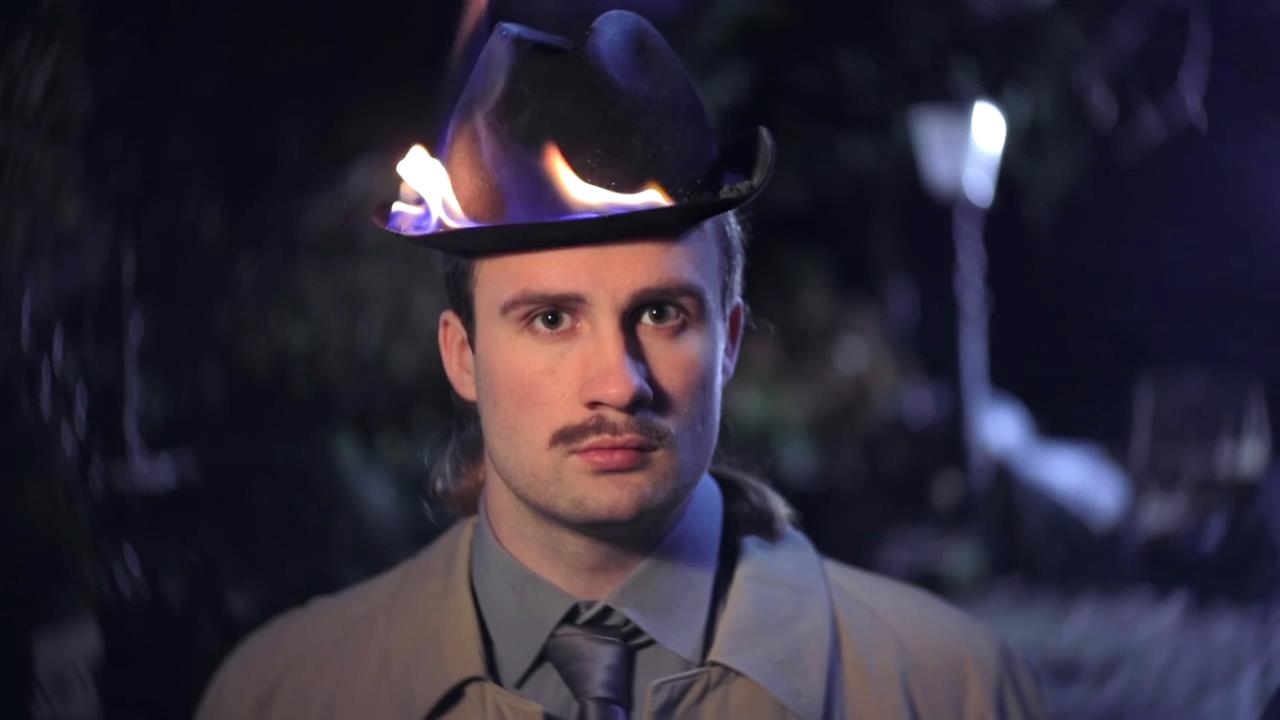 Szene aus "Maxwells Dämon" von Steven Hall. Ein junger Mann trägt einen schwarzen Hut, der am Rand brennt.