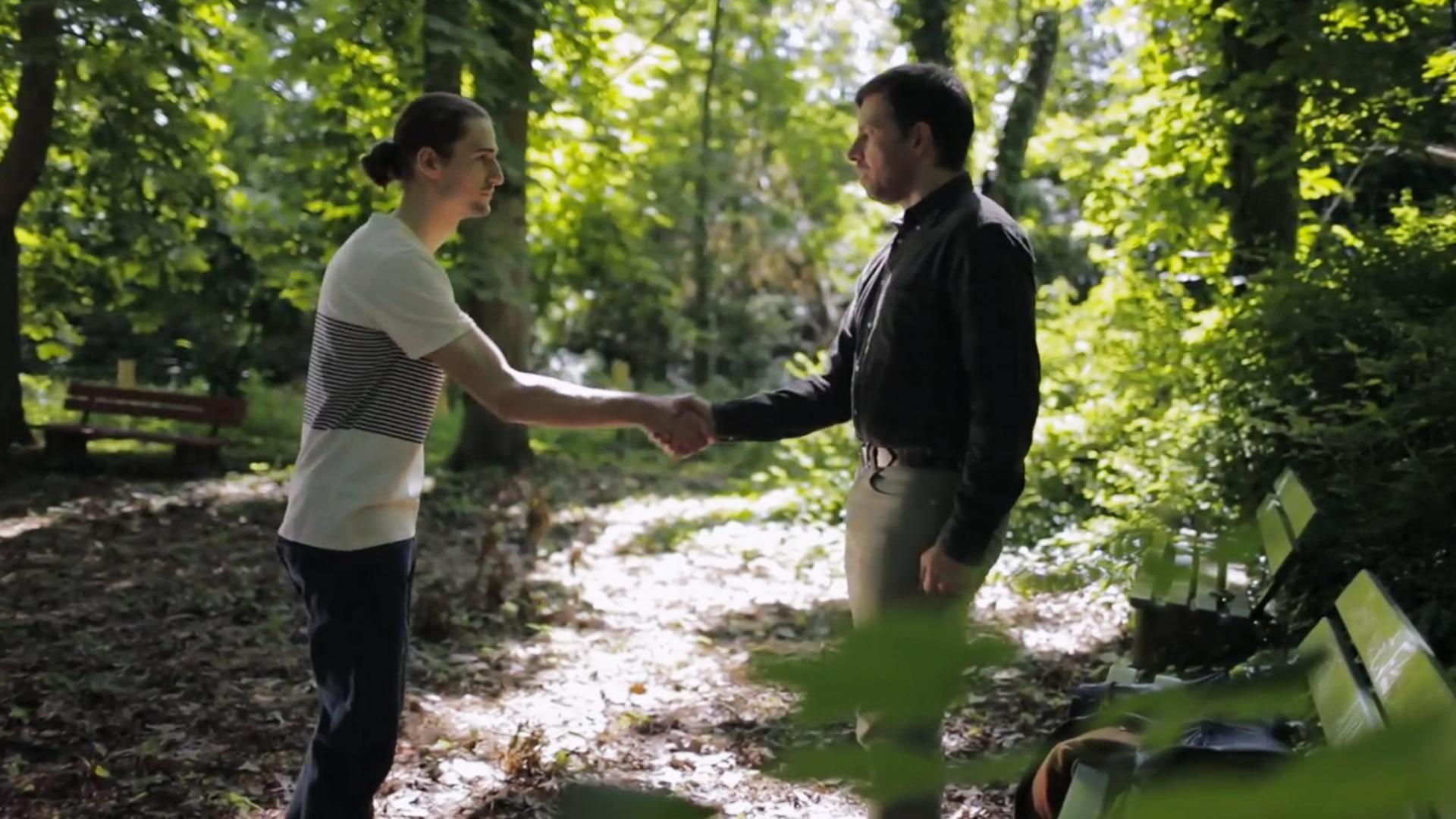 Szene aus "Humboldthain" von Inka Parei. Ein junger und älterer Mann stehen sich auf einem Walsweg gegenüber. Sie reichen sich die Hände.