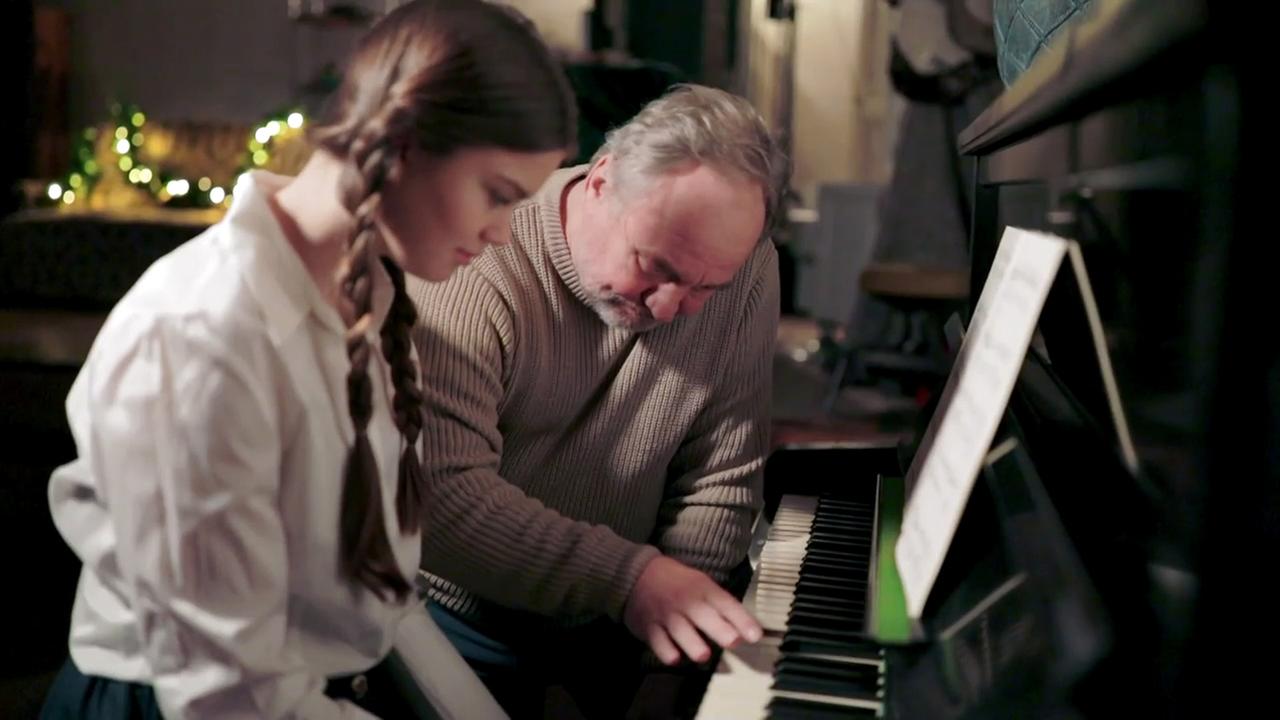 Szene aus "Die Enkelin" von Bernhard Schlink. Ein älterer Mann sitzt mit einer jungen Frau nebeneinander vor einem Klavier. Der Mann spielt der Frau etwas einhändig vor.