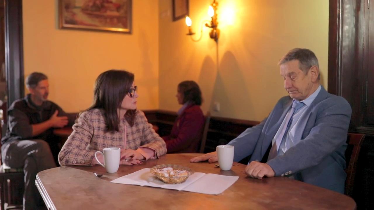 Szene aus "Oh, William!" von Elizabeth Strout. Eine Frau und ein Mann sitzen an einem Tisch und haben eine weiße Tasse vor sich.