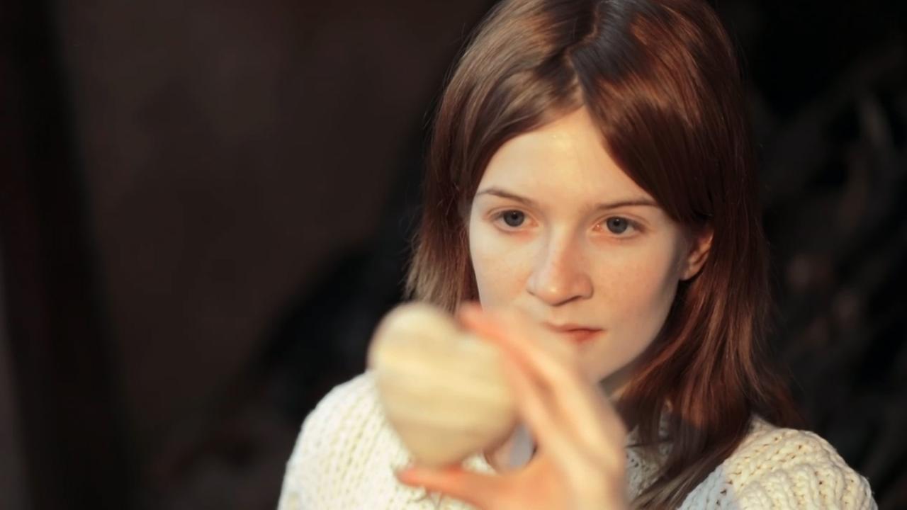 Szene aus "Der ganze Himmel" von Trent Dalton. Eine junge Frau hält ein Herz aus Stein auf Kinnhöhe in ihrer linken Hand und betrachtet es nachdenklich.