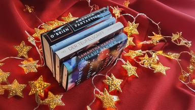 Vier Bücher auf einer roten Decke umgeben von einer Sternenlichterkette.