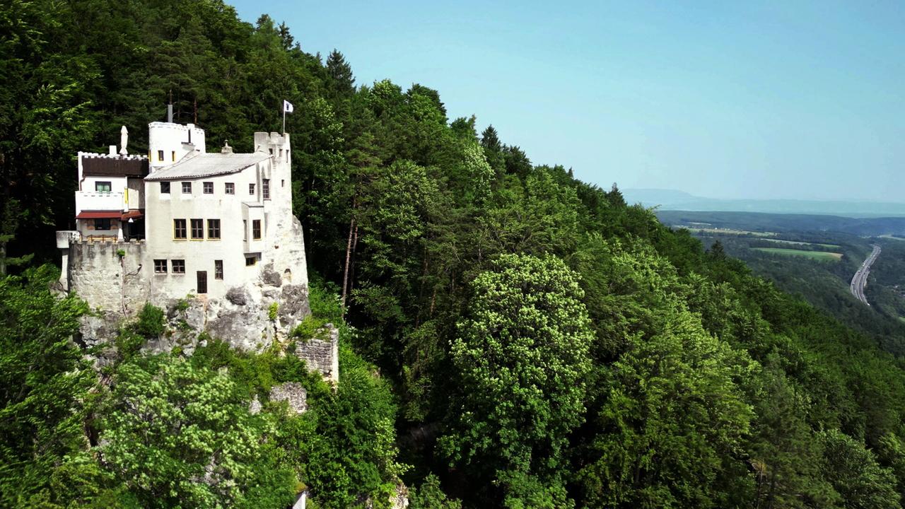 Eine weisse Burg auf einem Hügel im Wald