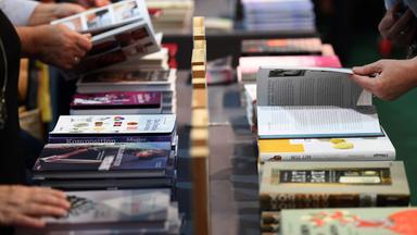 Auf einem Tisch liegen viele Bücher aus, welche sich mehrere Personen ansehen.