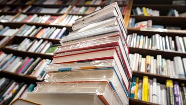 EIn Stapel Bücher steht vor einem großen Bücherregal.